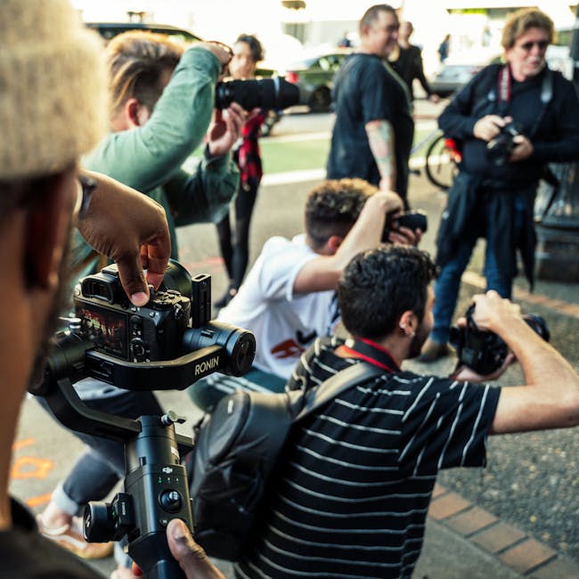 Group of photographers with cameras capturing an event outdoors during day.